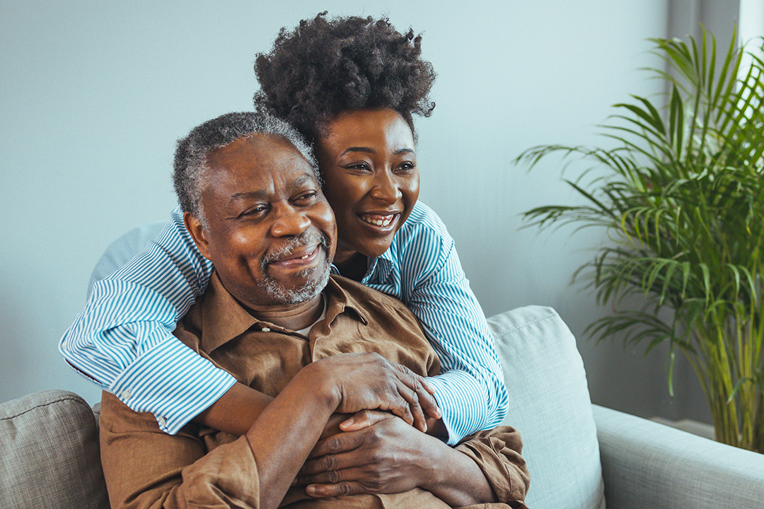 women hugging man from behind who is sitting on couch